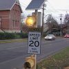 Closeup view of solar-powered school zone traffic beacon with amber flashing light above speed limit sign
