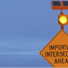 Important intersection ahead sign with amber round flashing light and solar panel.