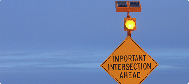 Important intersection ahead sign with amber round flashing light and solar panel.
