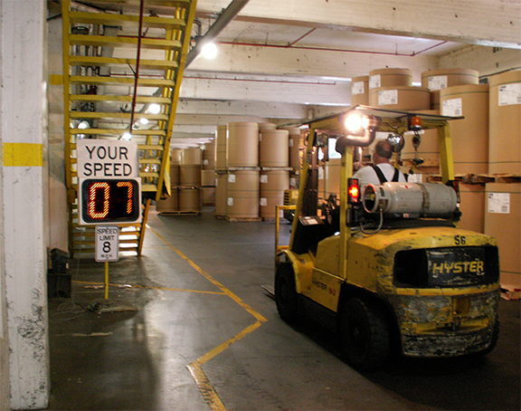 Forklift driving in warehouse full of containers with a Your Speed sign showing the drivers speed